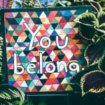 a sign that says you belong surrounded by plants
